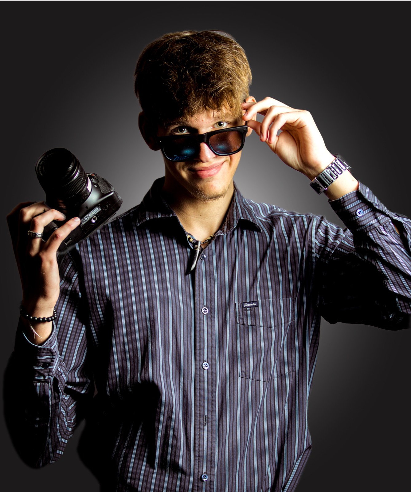 Ethan Adam holding a camera, smiling over the top of his sunglasses.